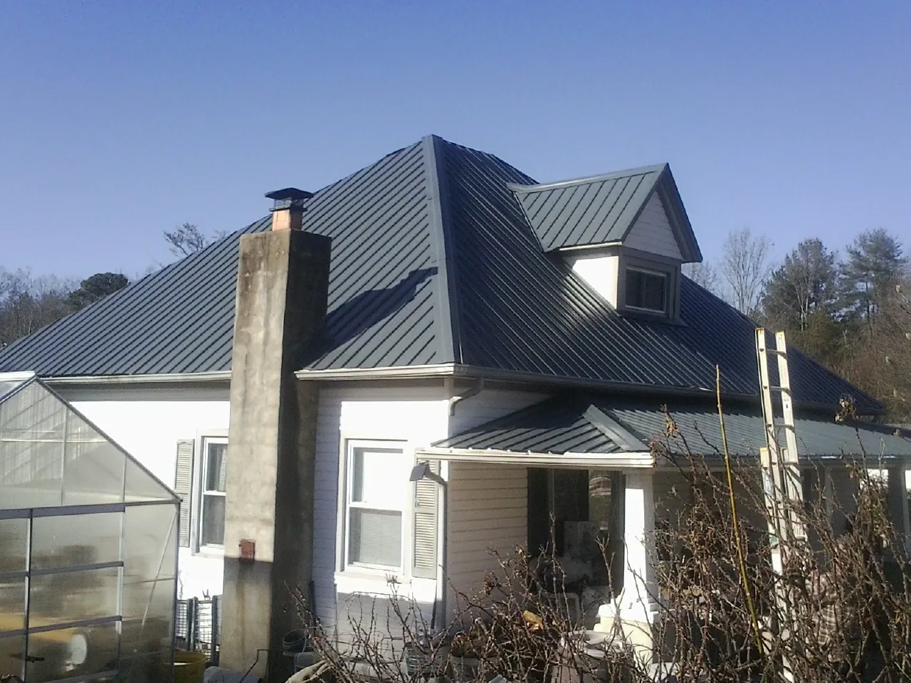 Dark blue standing seam metal roof on a white farmhouse with dormer — Slate & Tile Roof Repair by Roofing Brothers in Lynbrook