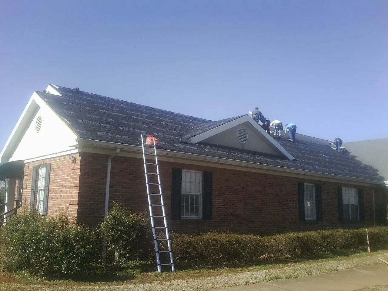 Crew tearing shingles off a brick ranch roof with a ladder set — Emergency Roof Repair work by our crew in Lynbrook