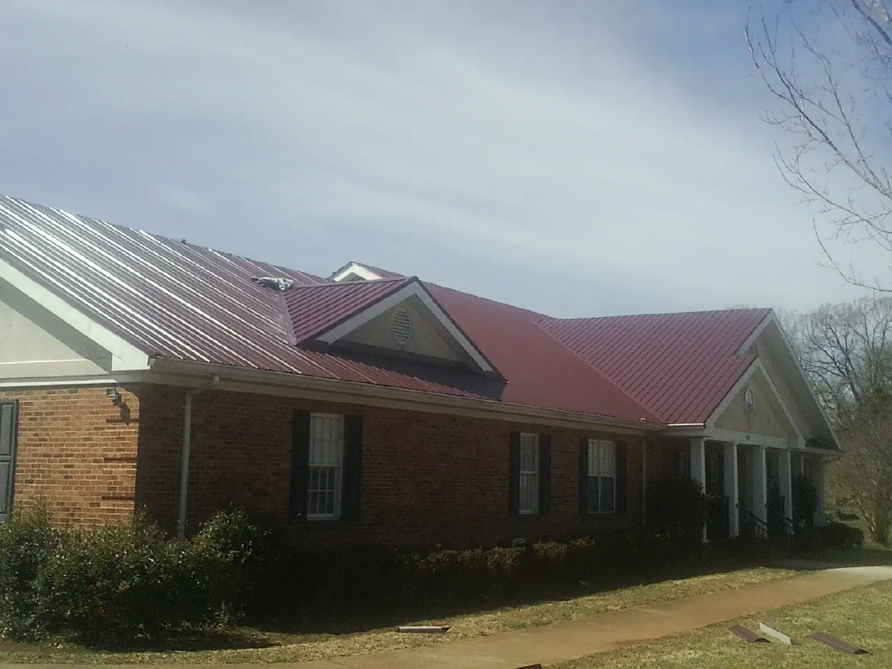 Red metal roof with gabled entries on a long brick building, from a Hail Damage Roof Repair job in Lynbrook
