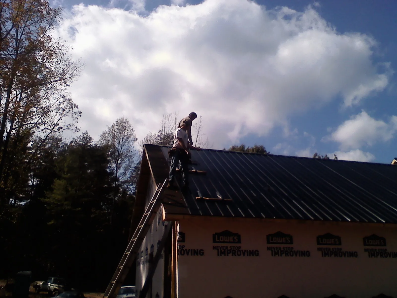 Roofer fastening dark metal panels high against a cloudy sky, from a Roof Inspection job in Lynbrook