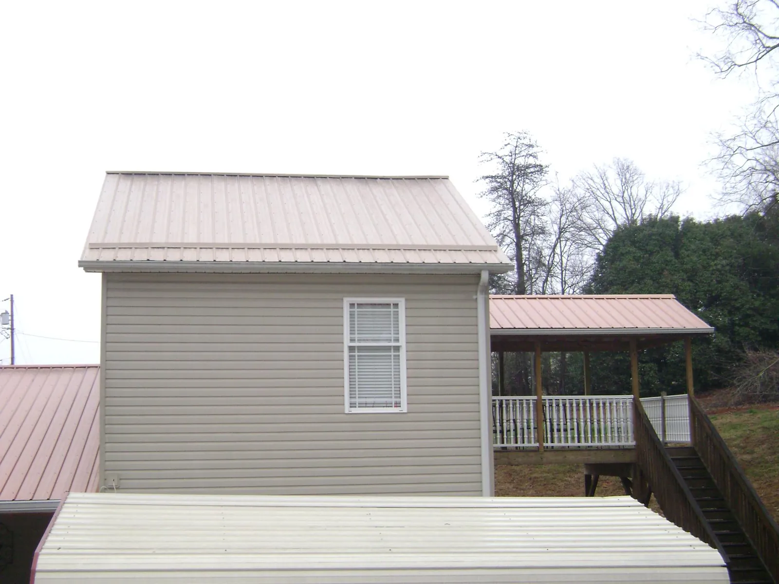 Tan metal roofs on a two story addition and attached porch, from a Roof Replacement job in Lynbrook